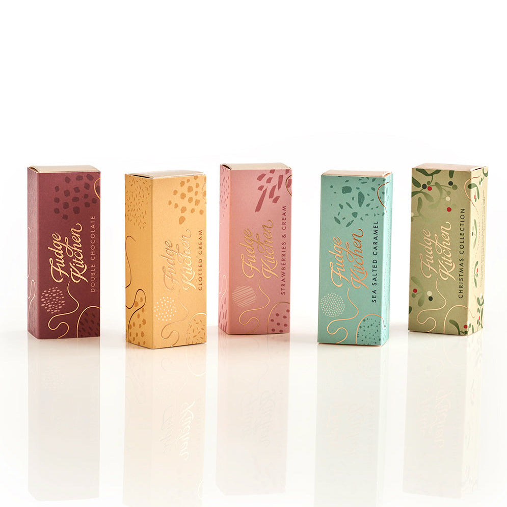 Five Fudge Kitchen gift boxes displaying trio slider boxes in Double Chocolate, Salted Caramel, Strawberries & Cream, Clotted Cream, and Festive Fudge flavours, arranged on a white surface.