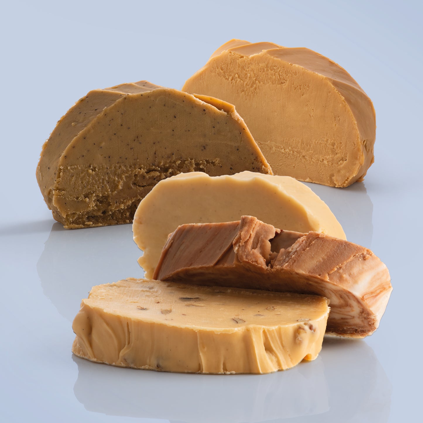 Five thick, fresh fudge slices on a reflective surface with a light blue background.