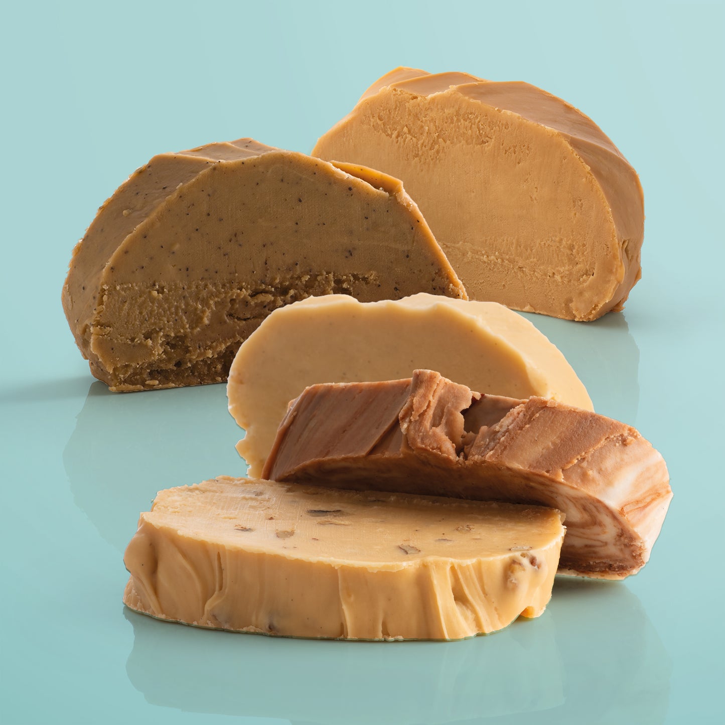 Five thick, fresh fudge slices on a reflective surface with a light blue background.