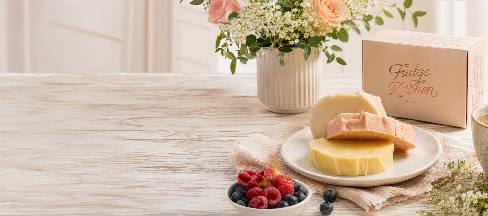 Slices of Fudge Kitchen fudge with a gift box, displayed on a cake board with flowers.