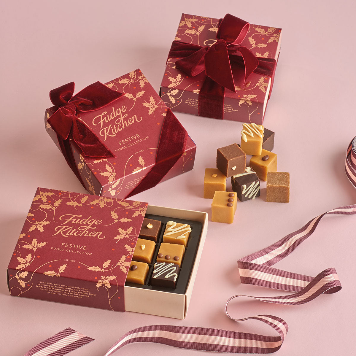 Fudge Kitchen festive fudge collection with red and gold packaging on a pink background