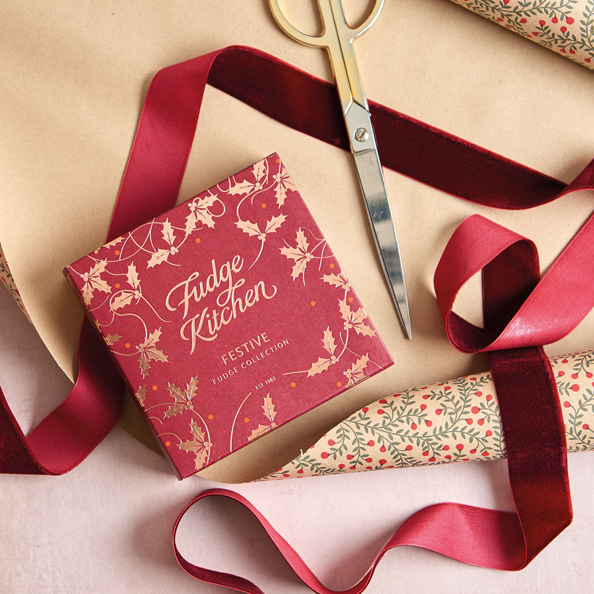 Fudge Kitchen festive product packaging with red ribbon and scissors on a beige surface