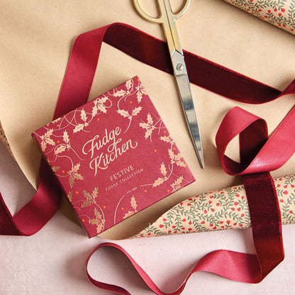 Fudge Kitchen festive product packaging with red ribbon and scissors on a beige surface