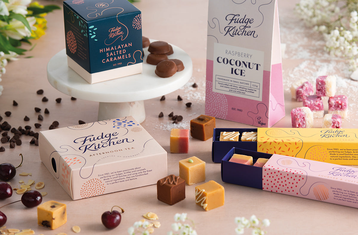 Fudge Kitchen confectionery boxes and treats on a table with flowers and cherries.