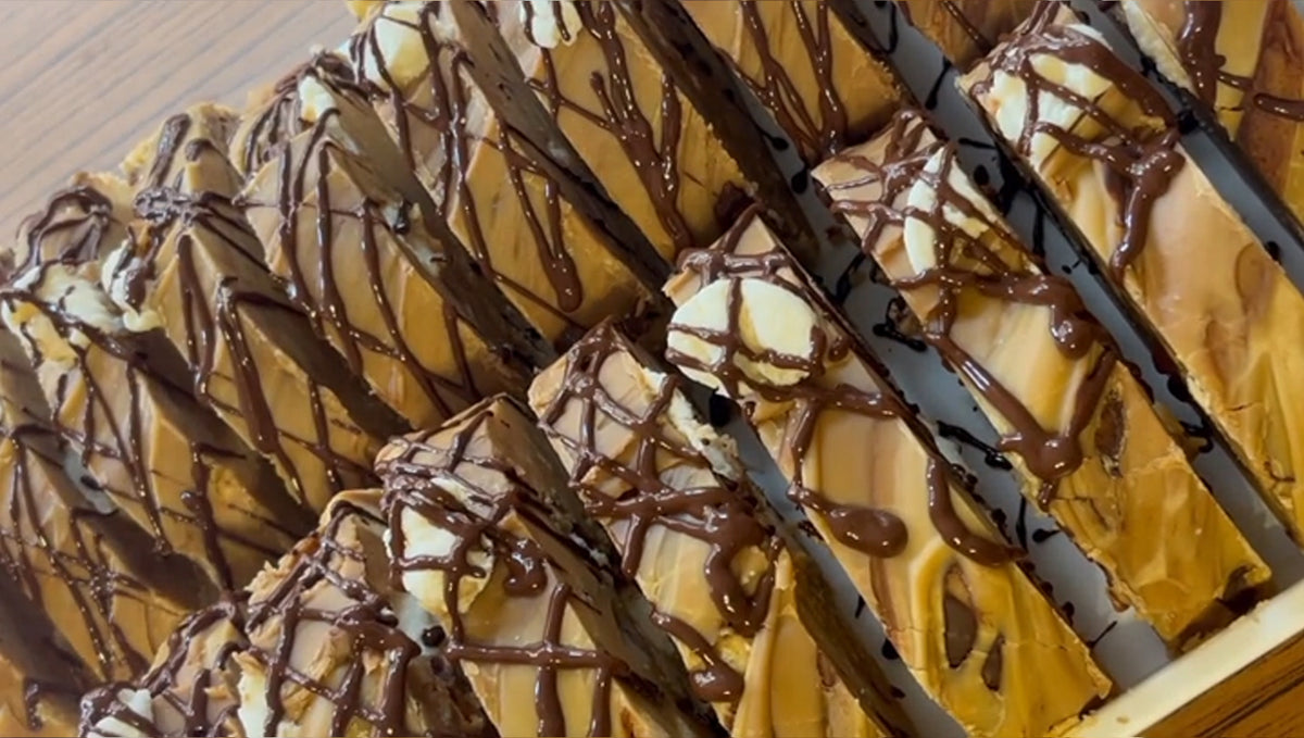 Close-up of s'mores fudge slices topped with chocolate drizzle, arranged in a tray on a wooden surface.
