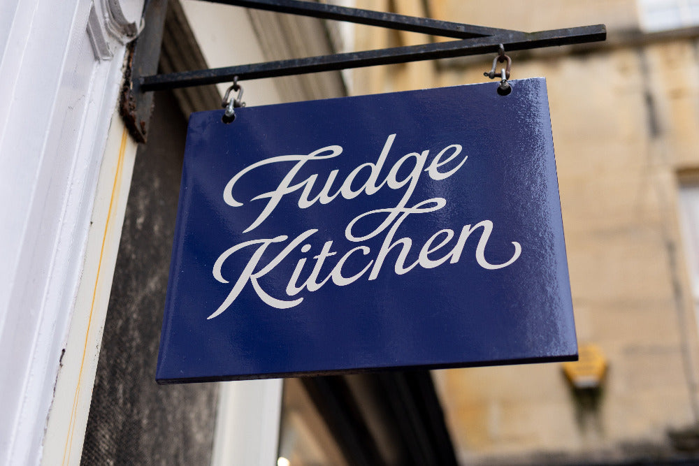 A close-up photo of the Fudge Kitchen hanging sign in fron of the Bath Fudge Kitchen shop