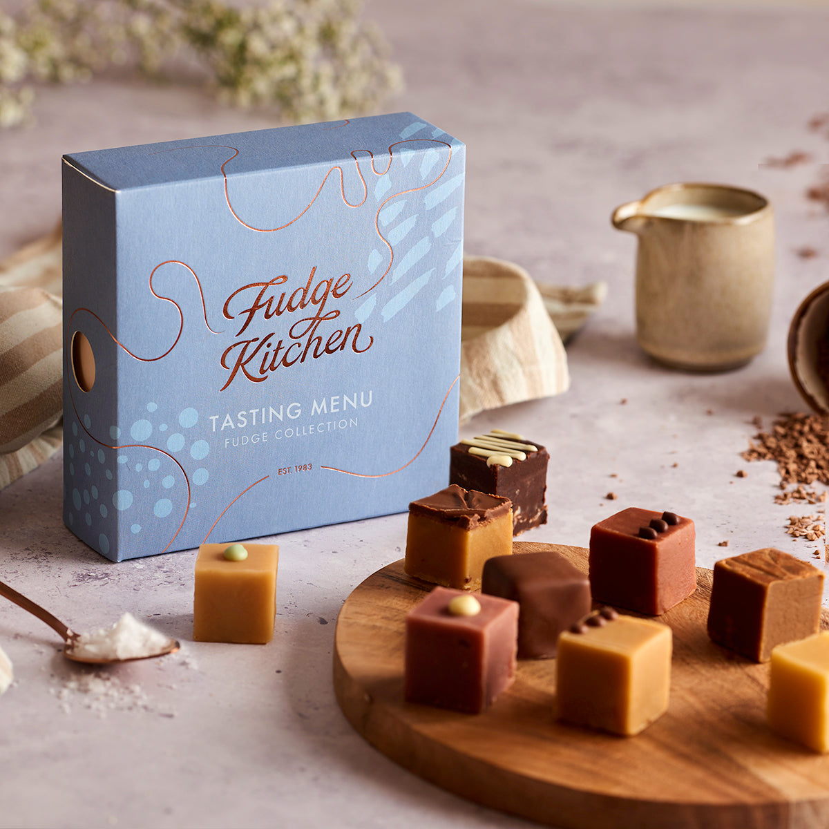 Fudge Kitchen Tasting Menu selection box featured in a table setting with artisan butter fudges displayed on a board and dining accoutrements.