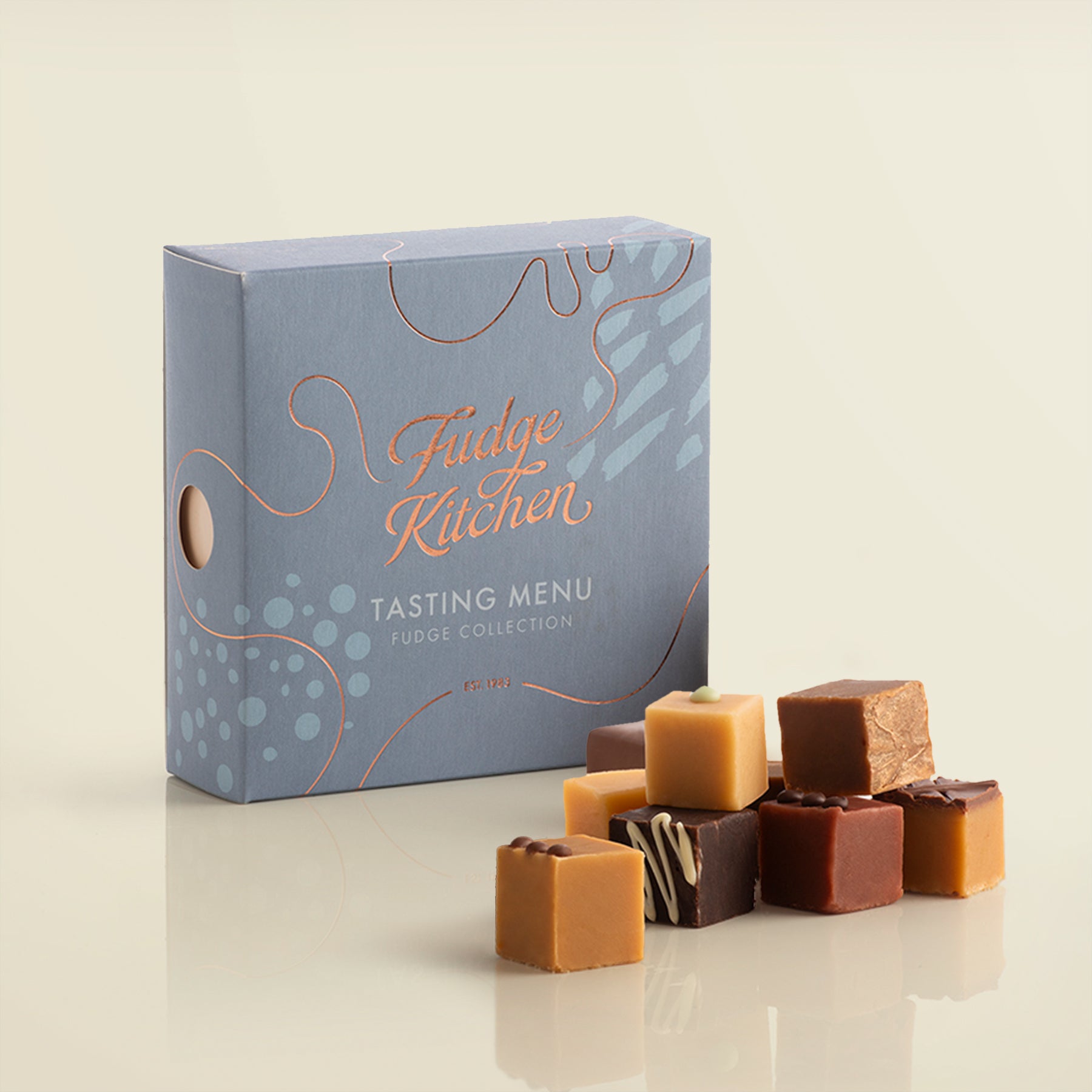 Fudge Kitchen, Tasting Menu Fudge Selection box, angled and featured on a light yellow background. Artisan fudge flavours displayed in a stack beside the box