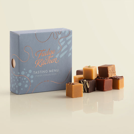Fudge Kitchen, Tasting Menu Fudge Selection box, angled and featured on a light yellow background. Artisan fudge flavours displayed in a stack beside the box