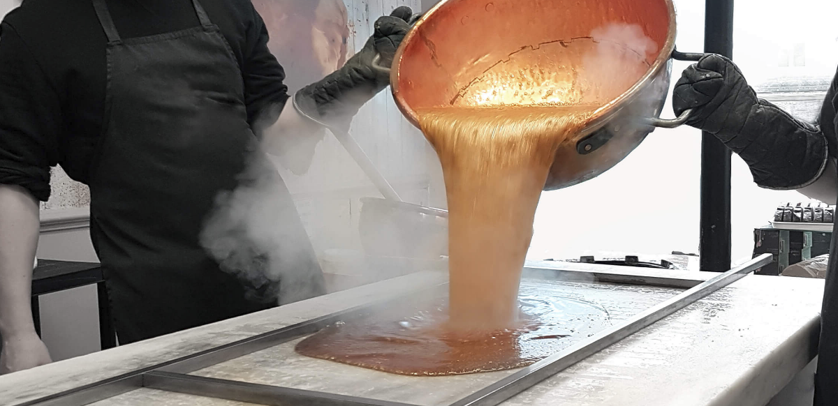 Person pouring a Fudge onto a marble table with steam rising, likely in a kitchen setting.