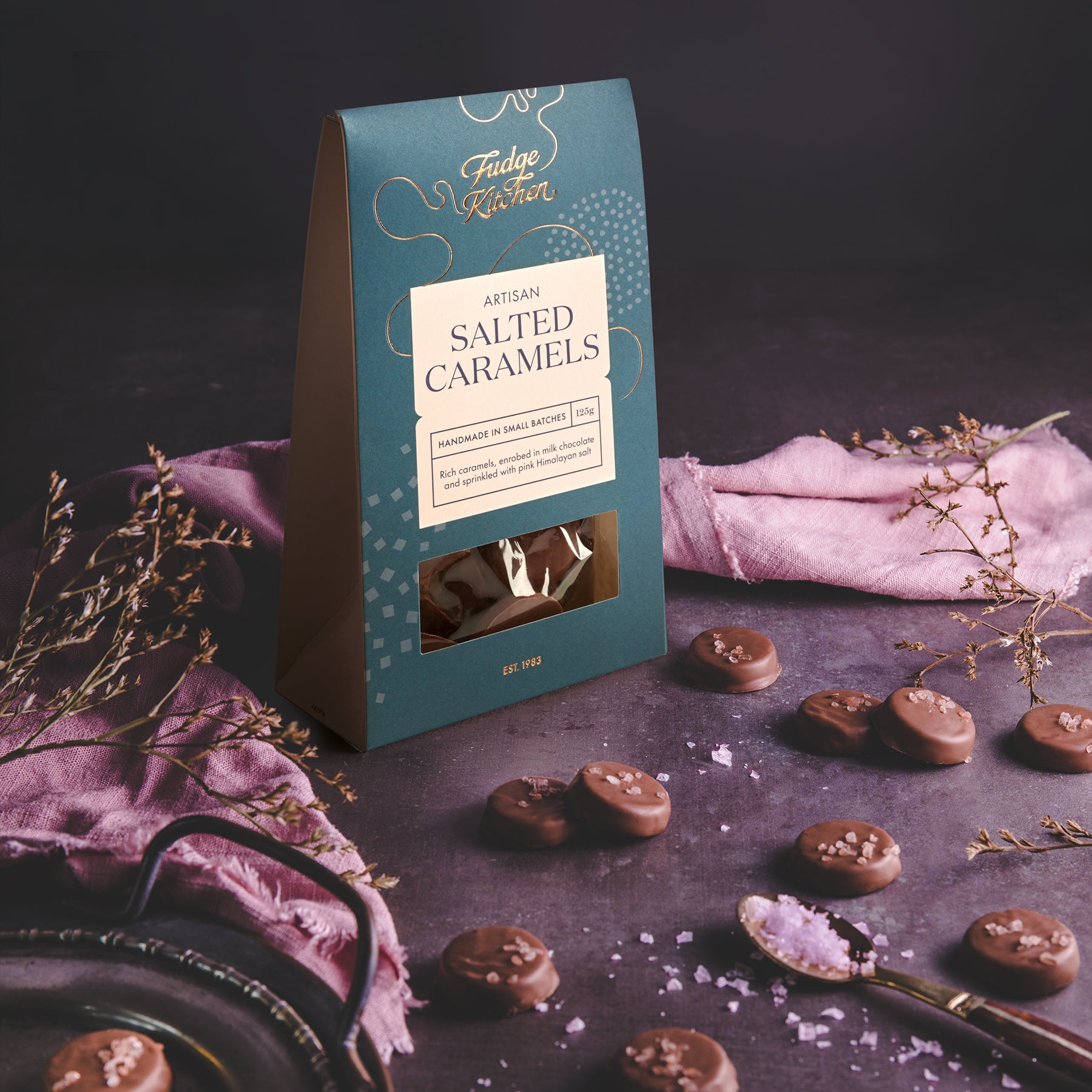 Packaging of Fudge Kitchen salted caramels on a dark surface with caramels around