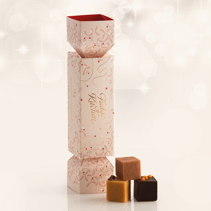 Luxury christmas cracker box with a subtle mistletoe design and 3 fudge pieces in front on a sparkle background.