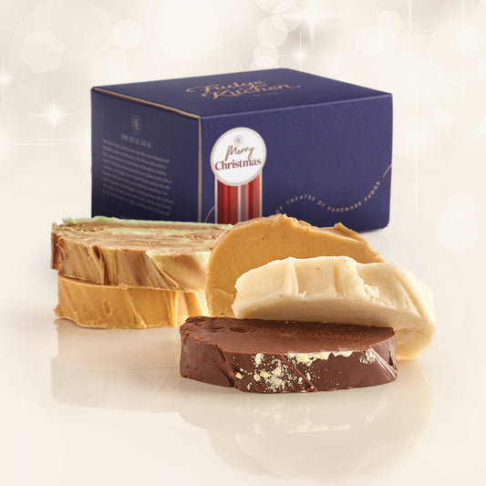 Christmas Fudge Selection showing 5 slices of fresh fudge in christmas flavours ldisplayed on a plain background with a luxury gift box behind with a Christmas Gift with Decorative Seal