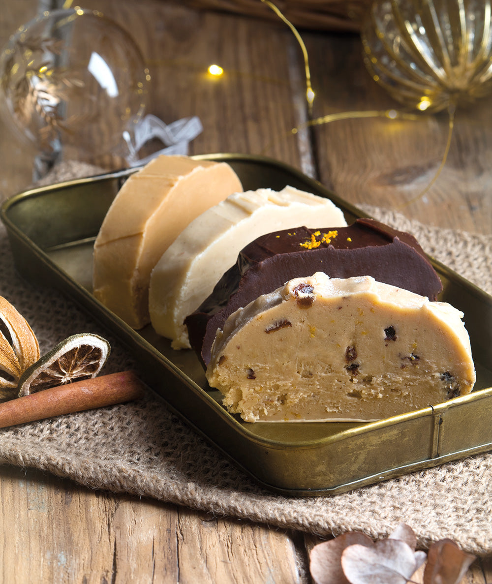 Delicious Christmas Fudge Gift Selection of fudge slices in a range of flavours, displayed on a metal tray and christmas deorations in the background.