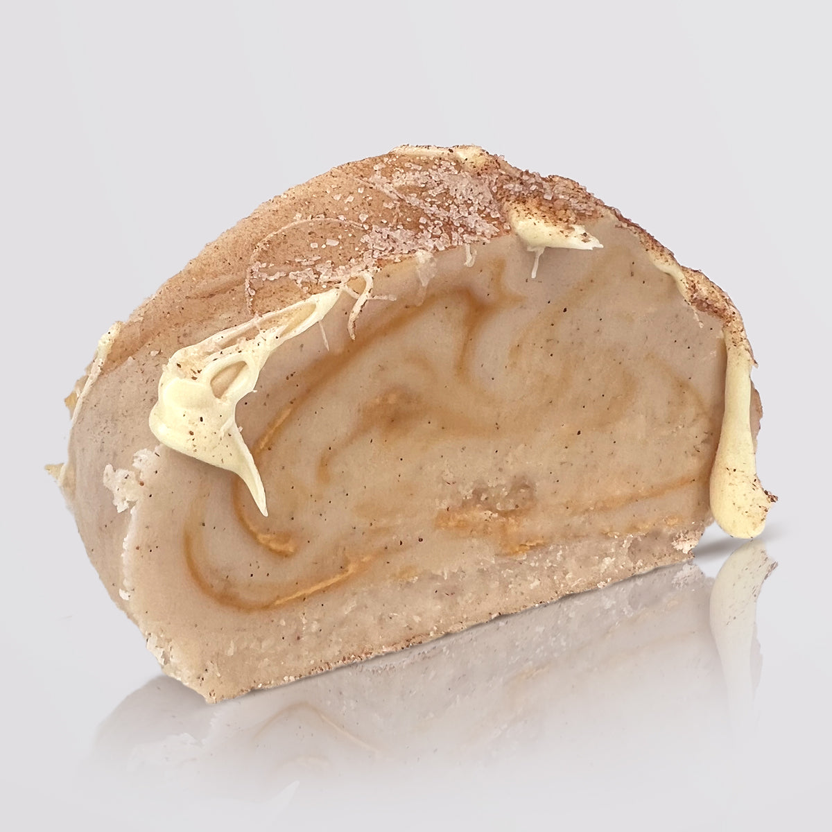 A single slice of cinnamon bun fudge, with drizzles of white chocolate, photographed on a clean light gray background with a soft reflection below.