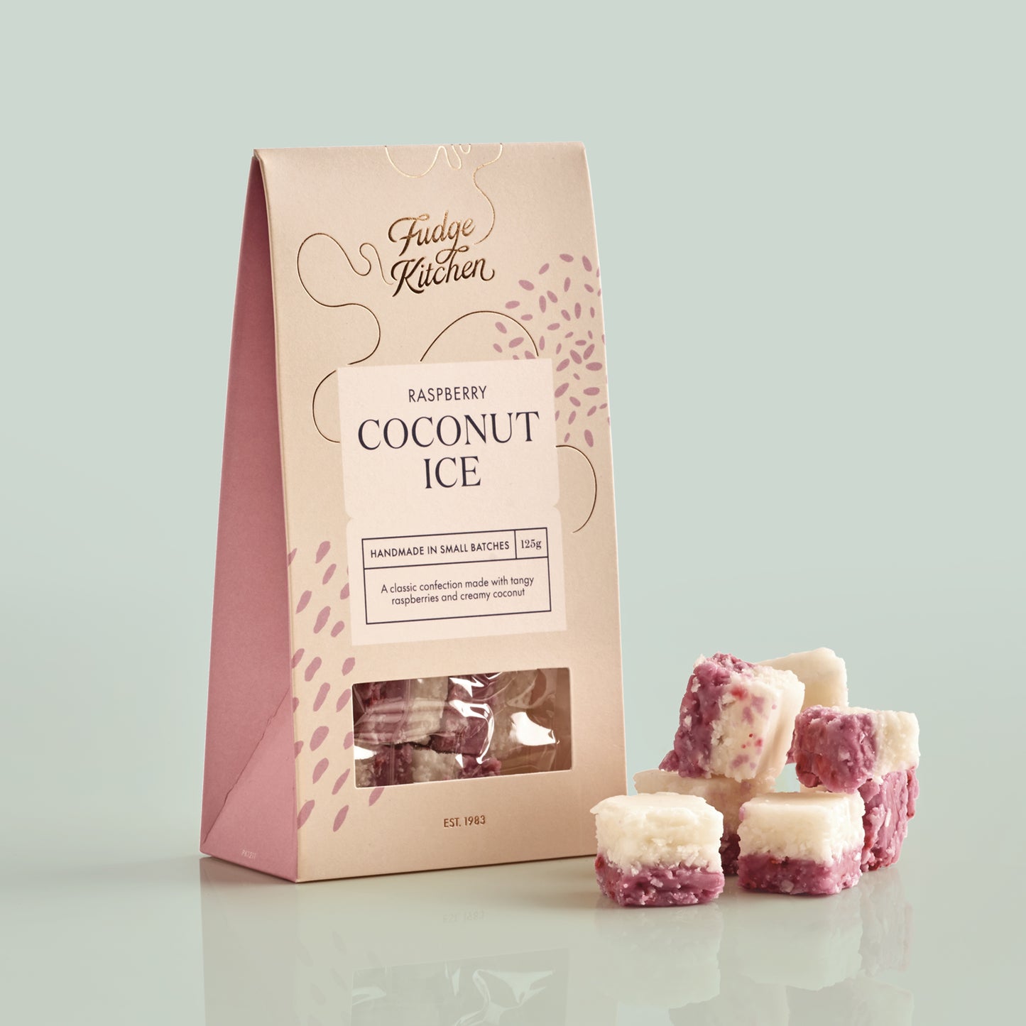 Fudge Kitchen raspberry coconut ice packaging with fudge pieces on a light green background