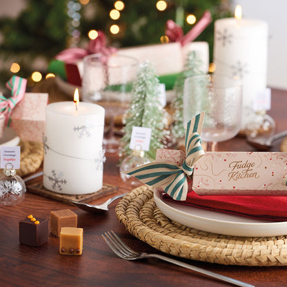 Christmas-themed table setting with candles, plates, and decorative items with luxury fudge crackers and 3 pieces of gourmet fudge.
