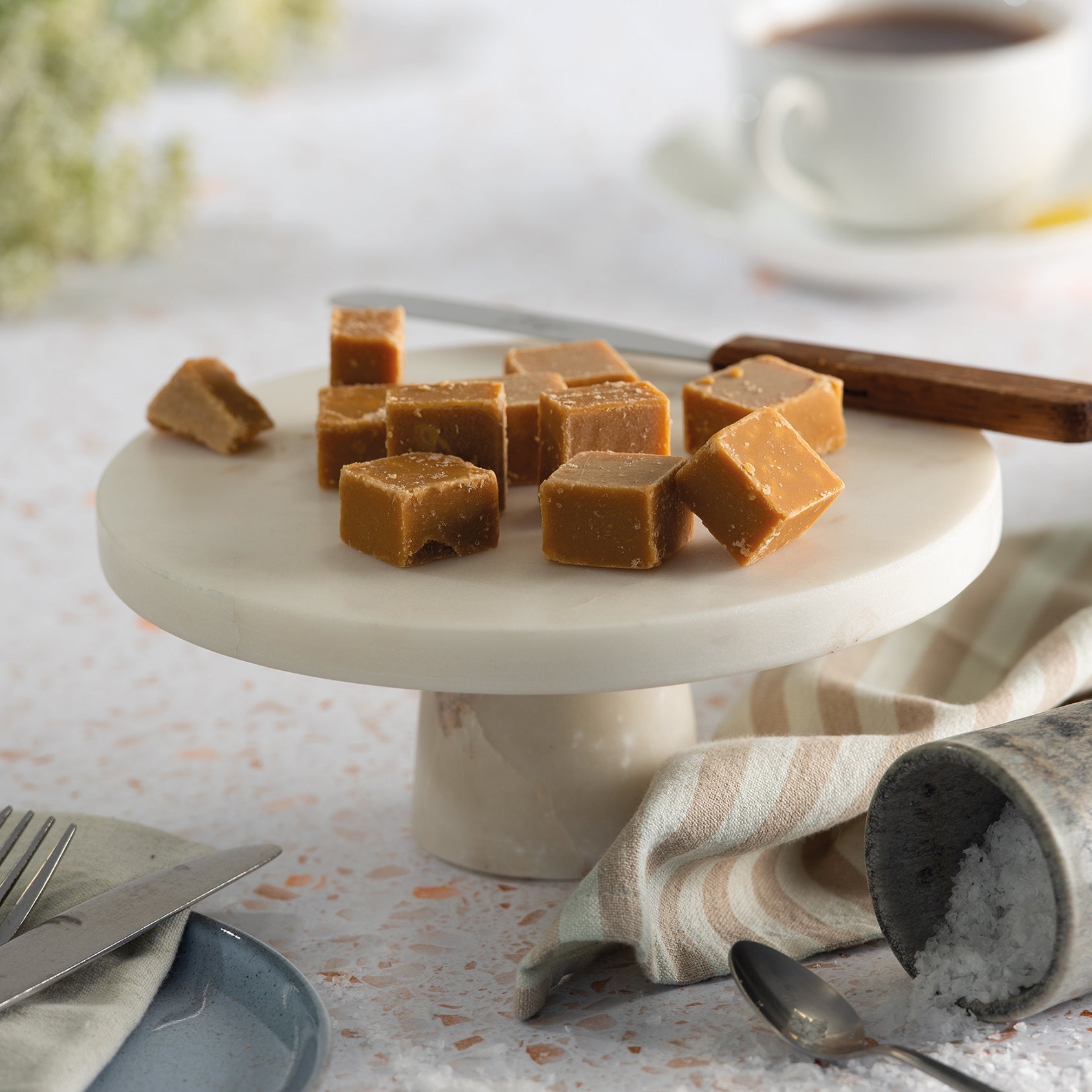 Salted caramel fudge pieces on a marble stand with a cup of tea in the background