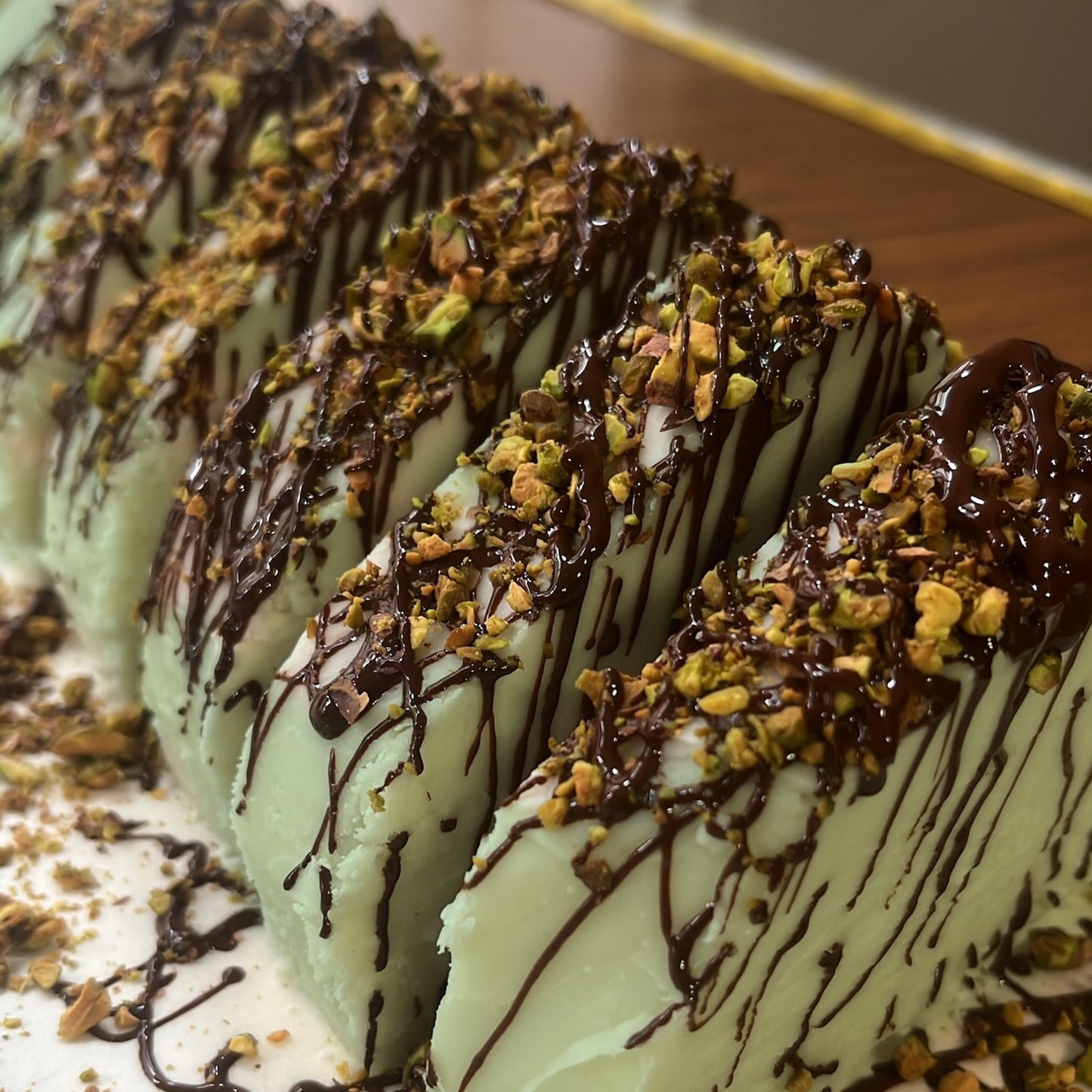 A close-up of a tray of slices of dubai style fudge, drizzled with dark chocolate, and topped with chopped nuts.