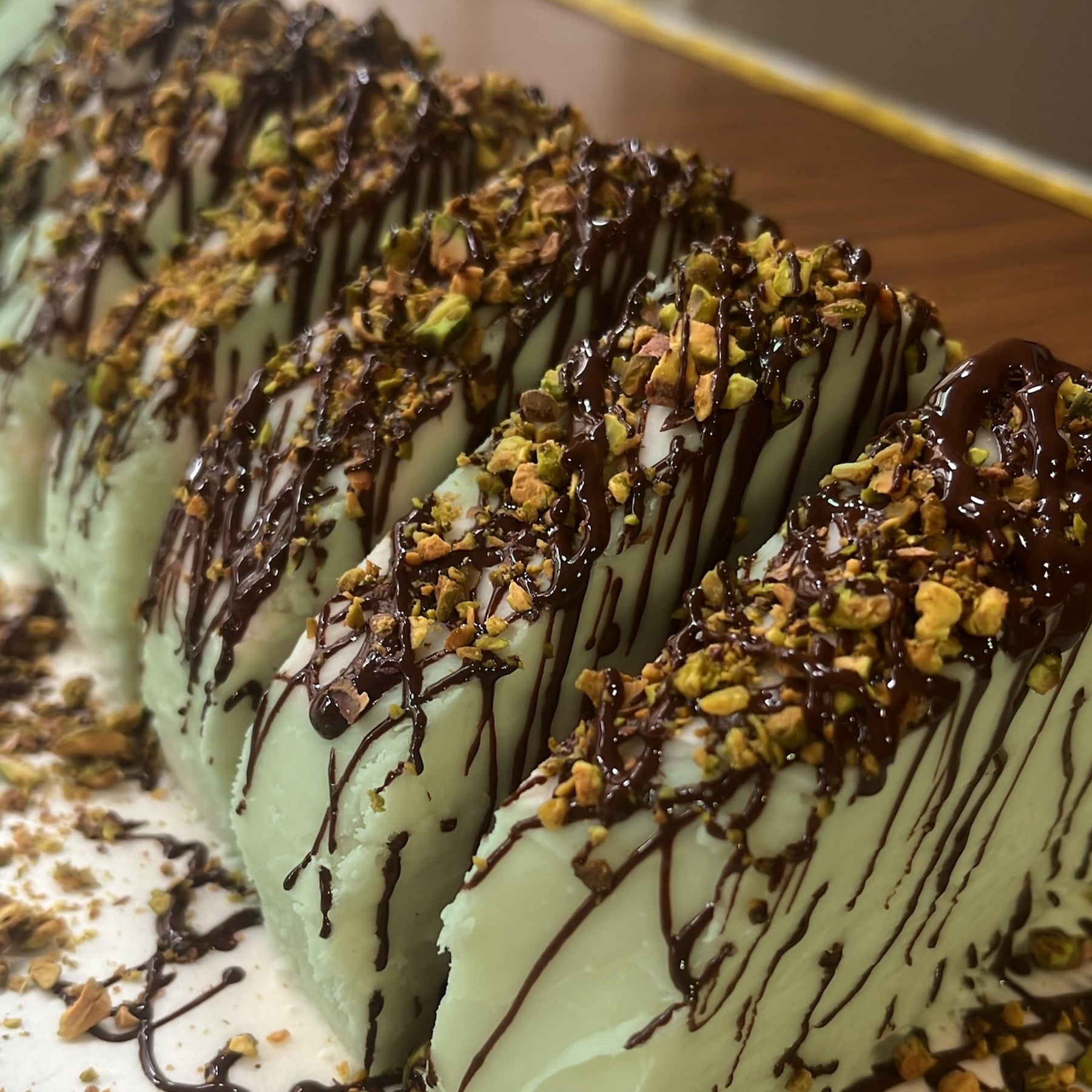 A close-up of a tray of slices of dubai style fudge, drizzled with dark chocolate, and topped with chopped nuts.