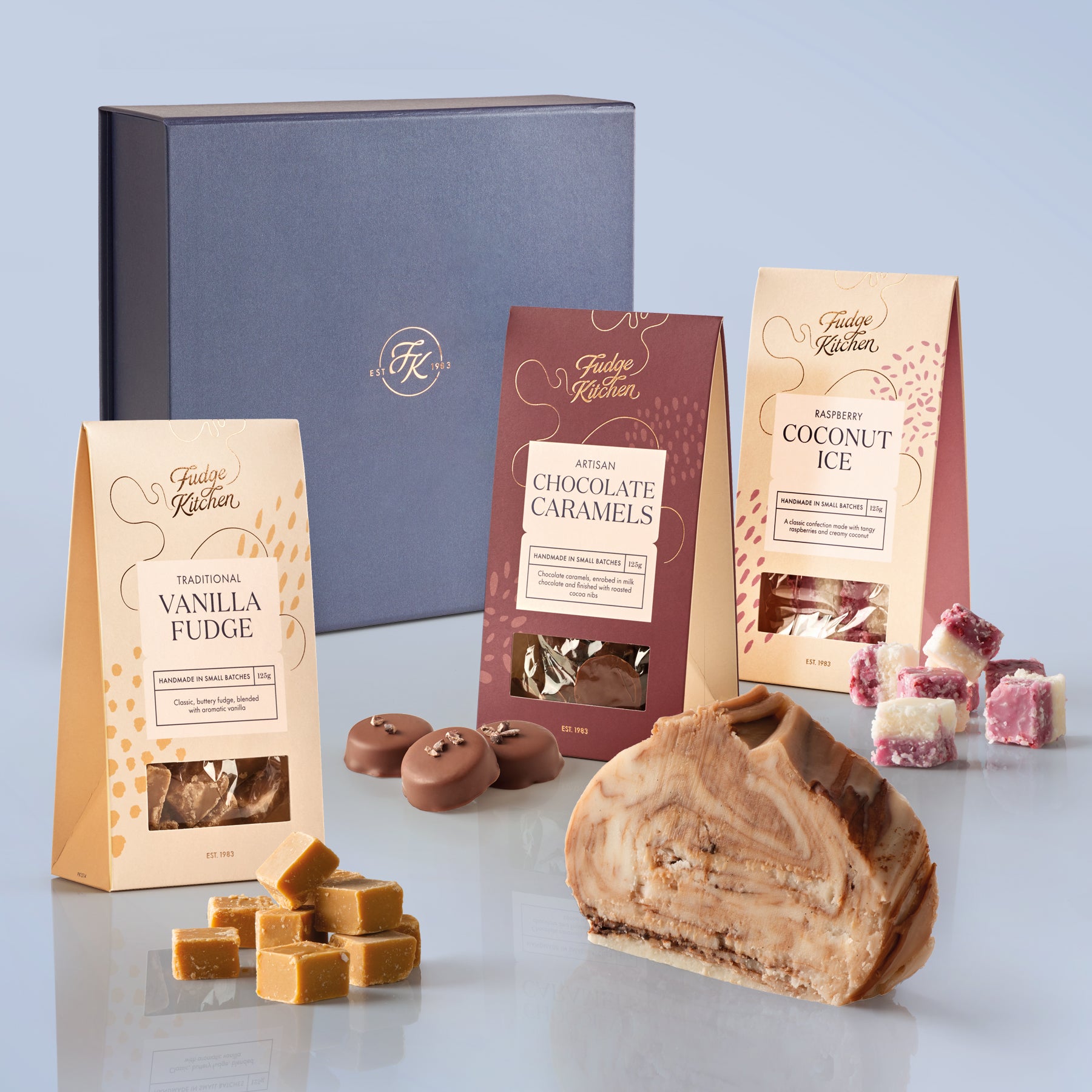 Assorted Fudge Kitchen confectionery items including fudge, caramels, and coconut ice on a light blue background.