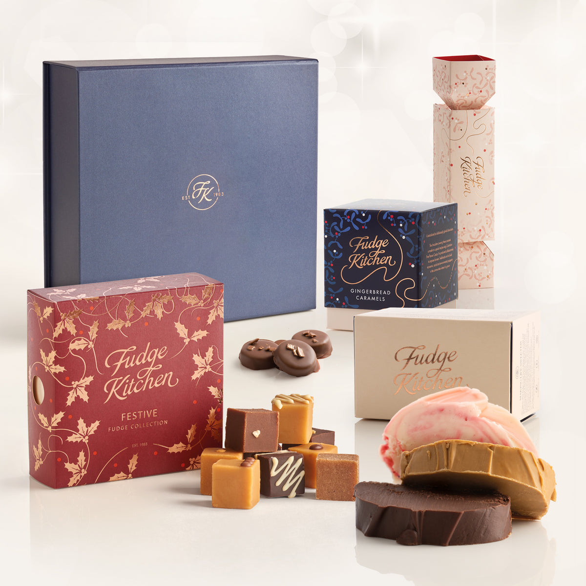 Fudge Kitchen Christmas Luxury Hamper gift set with multiple gift selections, including gingerbread caramels, festive 9 piece selection and a three slice fudge box, arranged with assorted fudges, caramels, and a decorated fudge slices on a clean white background.