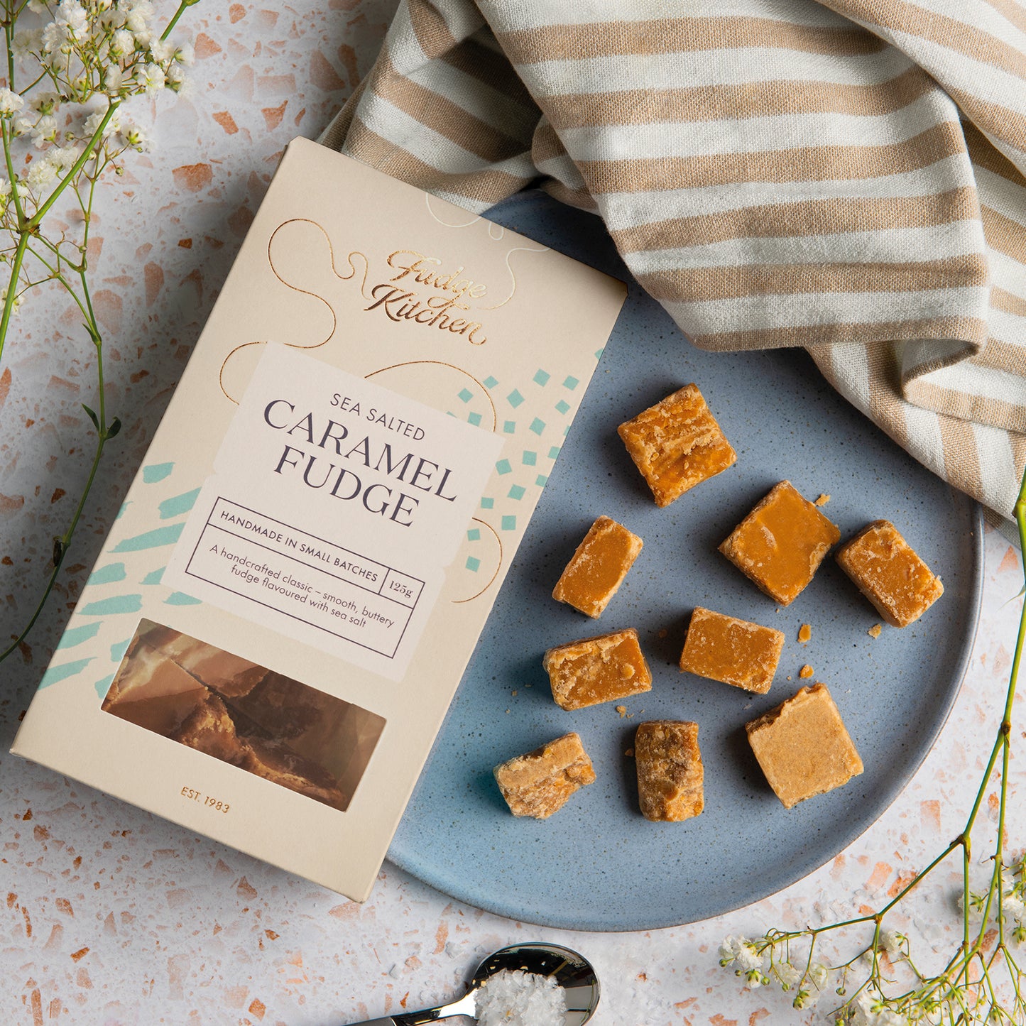 Fudge Kitchen sea salted caramel fudge on a plate with packaging and a striped cloth.