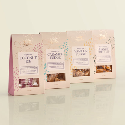 Four packages of Fudge Kitchen artisan confectionary gift packs on a reflective surface with a light background