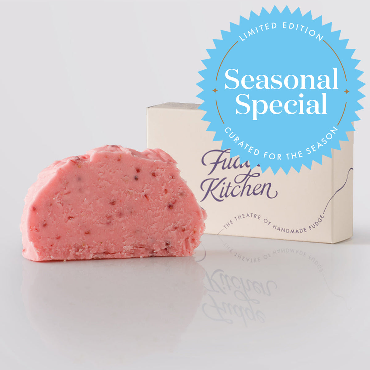 A pink raspberry sorbet flavoured fudge slice with visible red fruit pieces, displayed next to its buff gift box. A blue circular badge on the top right reads 'Seasonal Special' and 'Curated for the Season' by 'Fudge Kitchen'.