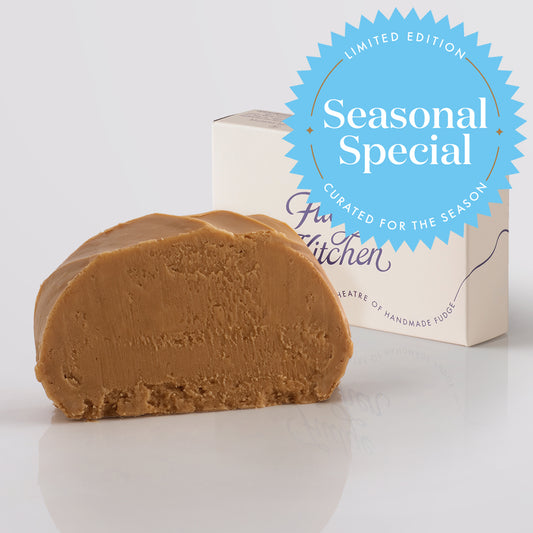 A single slice of handmade butterscotch fudge is shown in front of its cream-coloured packaging box, with a blue 'Seasonal Special' promotional badge overlaid in the upper right. The box features the brand name 'Fudge Kitchen'.