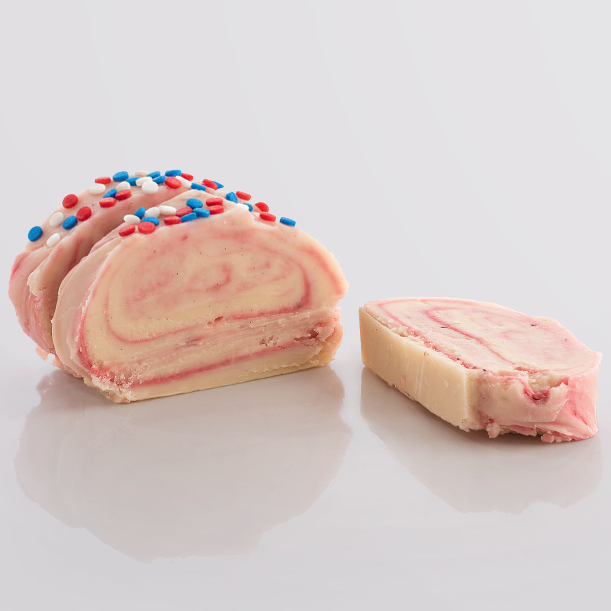 Swirled fudge with pink and white layers and red, white, and blue sprinkles on a light grey background.