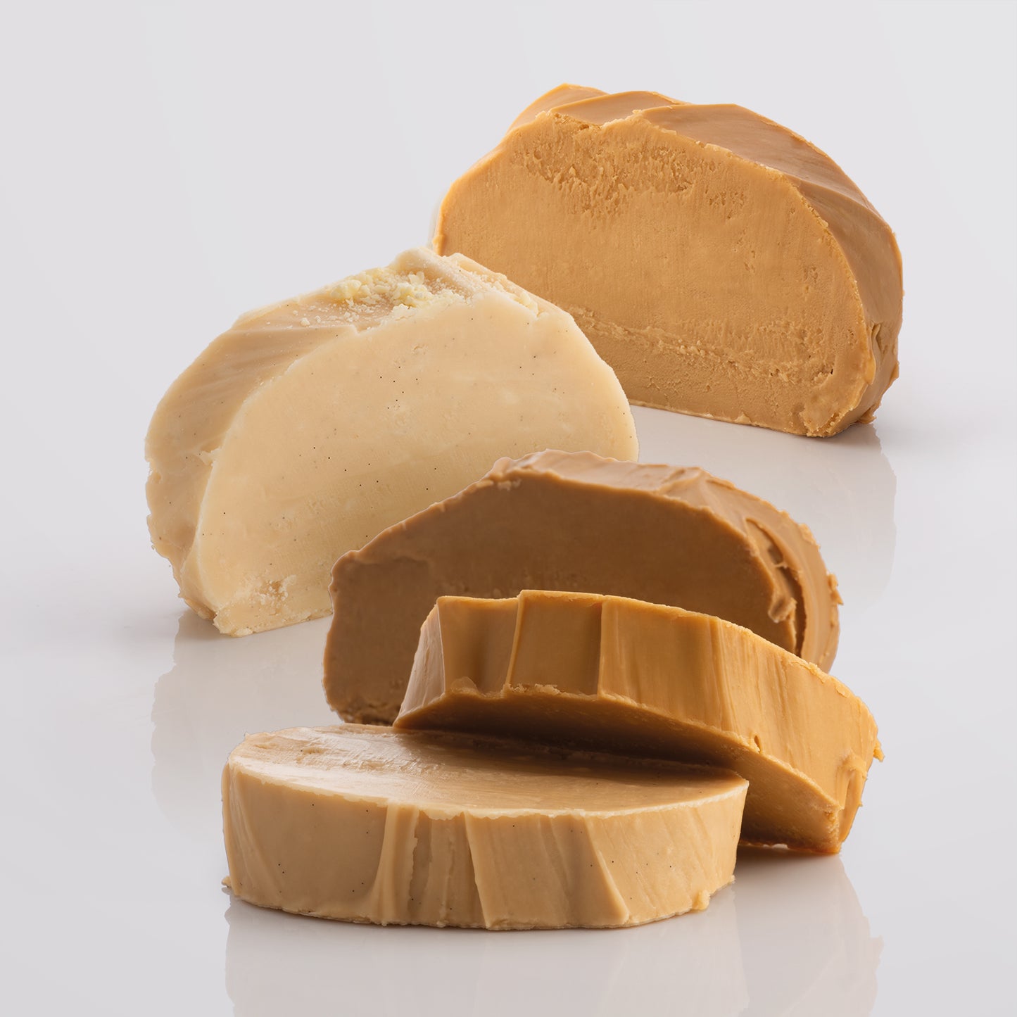 Five thick, fresh fudge slices on a reflective surface with a light gray background.