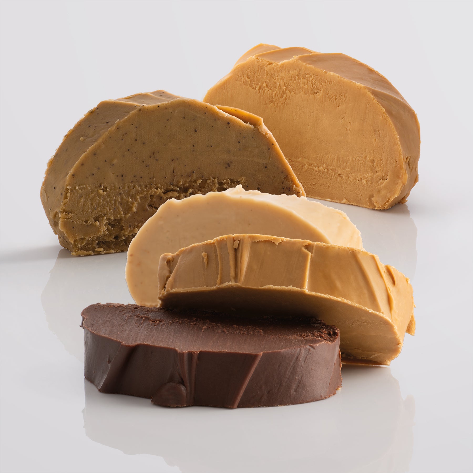 Five thick, fresh fudge slices on a reflective surface with a light gray background.