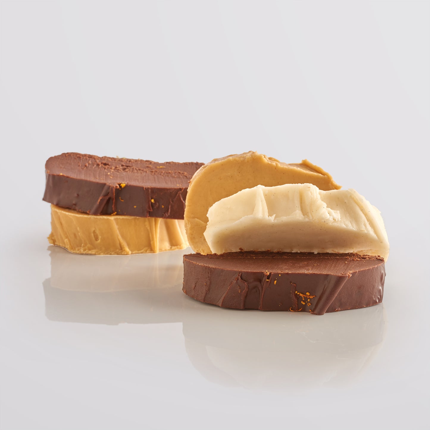 Five thick, fresh fudge slices on a reflective surface with a light gray background.