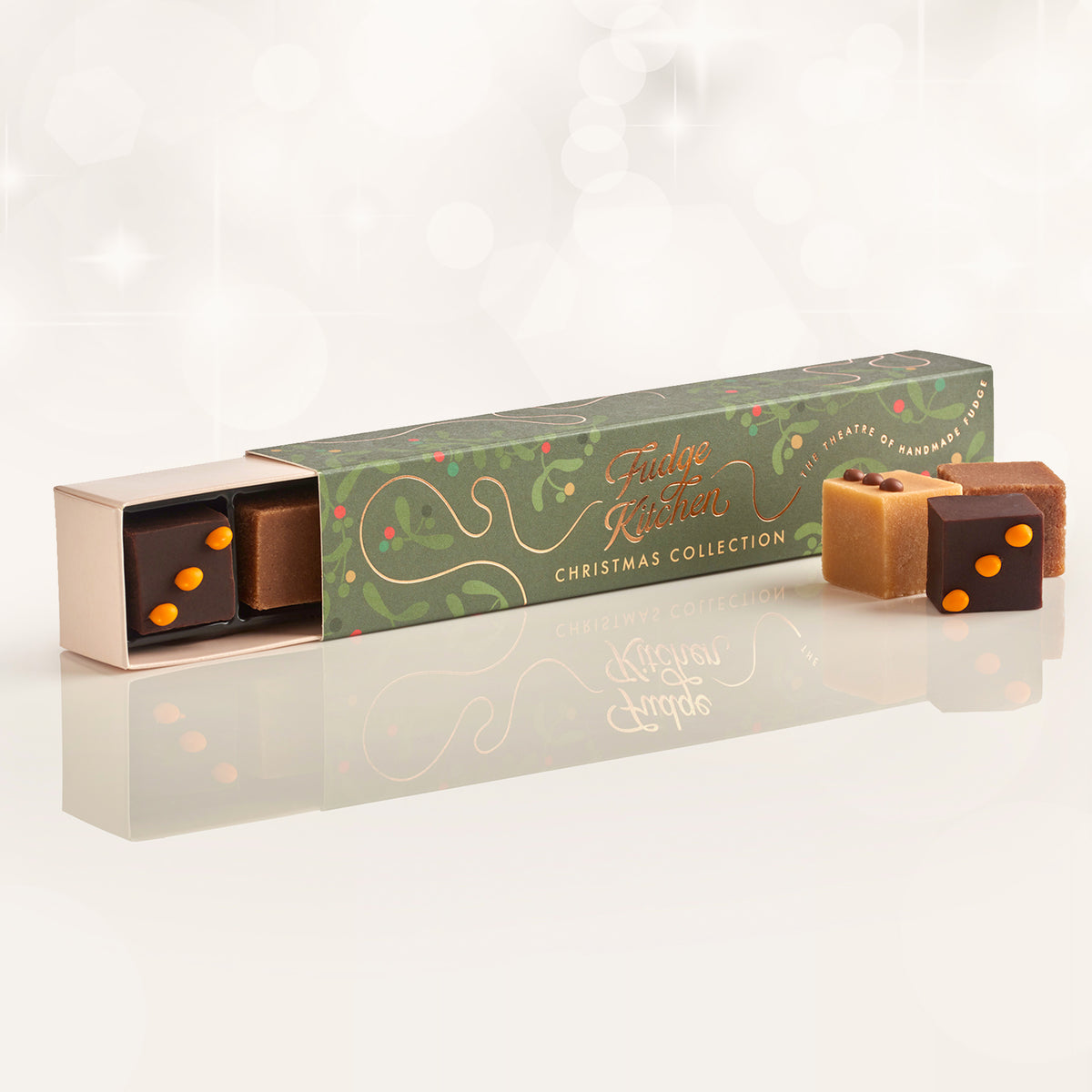 Christmas fudge packaging with 'Fudge Kitchen' branding, slightly open to reveal a piece of chocolate & orange fudge, with three pieces of artisan fudge in front of the long box on a reflective background.