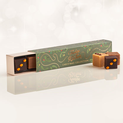 Christmas fudge packaging with 'Fudge Kitchen' branding, slightly open to reveal a piece of chocolate & orange fudge, with three pieces of artisan fudge in front of the long box on a reflective background.