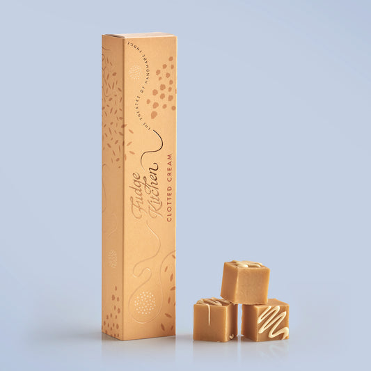 Three pieces of Fudge Kitchen clotted cream fudge stacked in front of a tall gift box on a light blue background.