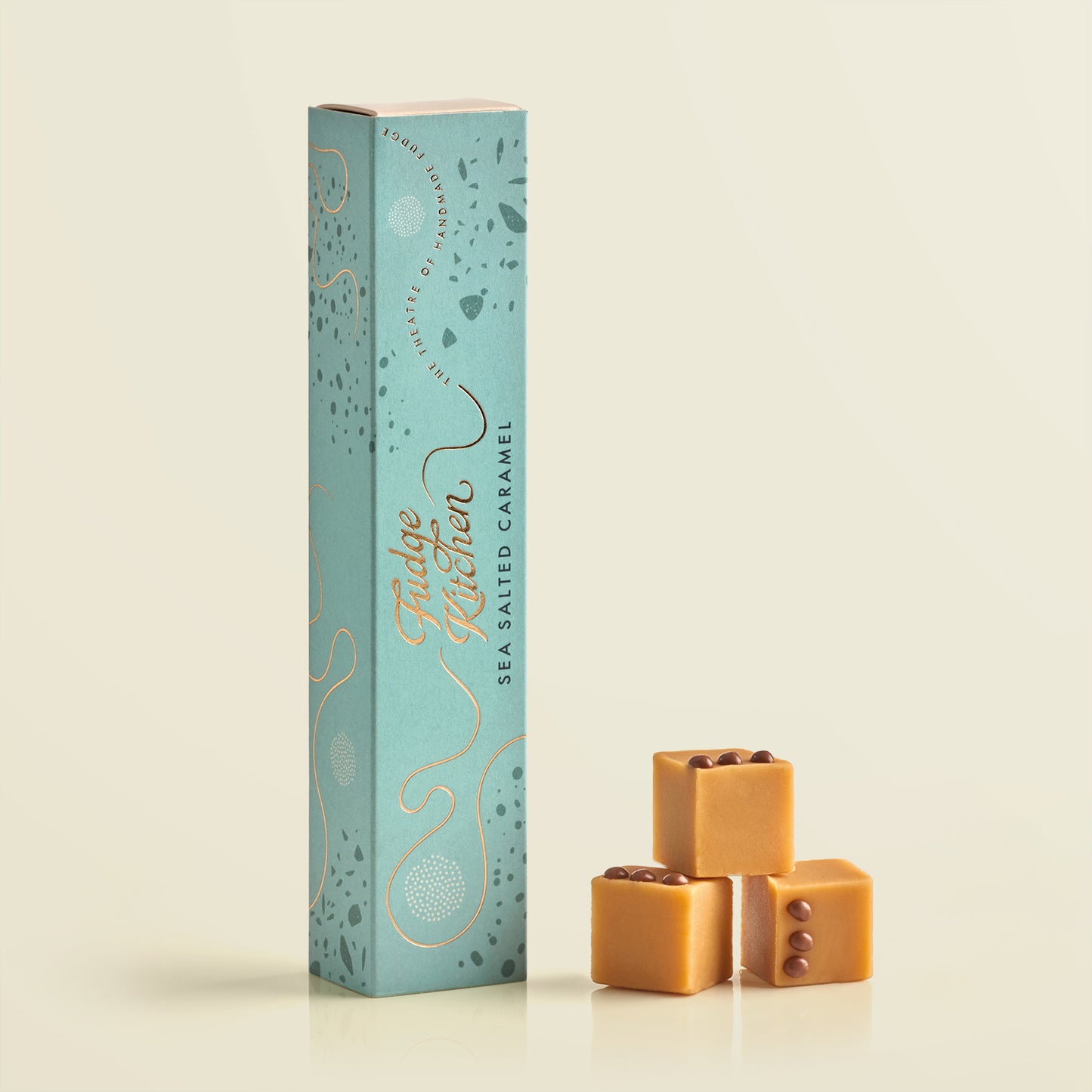 Tall teal box with 'Fudge Kitchen' branding next to three sea salted caramel fudges on a light beige background