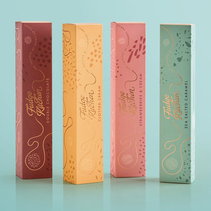 Four Fudge Kitchen fudge gift boxes in different colors on a light blue background