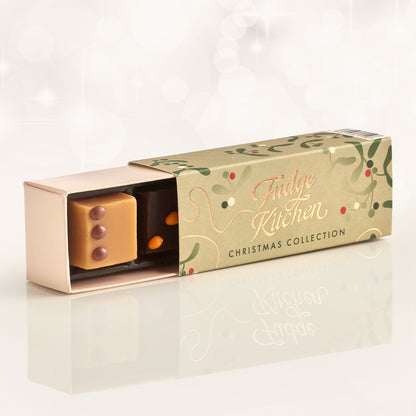 Festive fudge packaging with 'Fudge Kitchen' branding, slightly open to reveal a piece of salted caramel and chocolate & orange on a pale background.