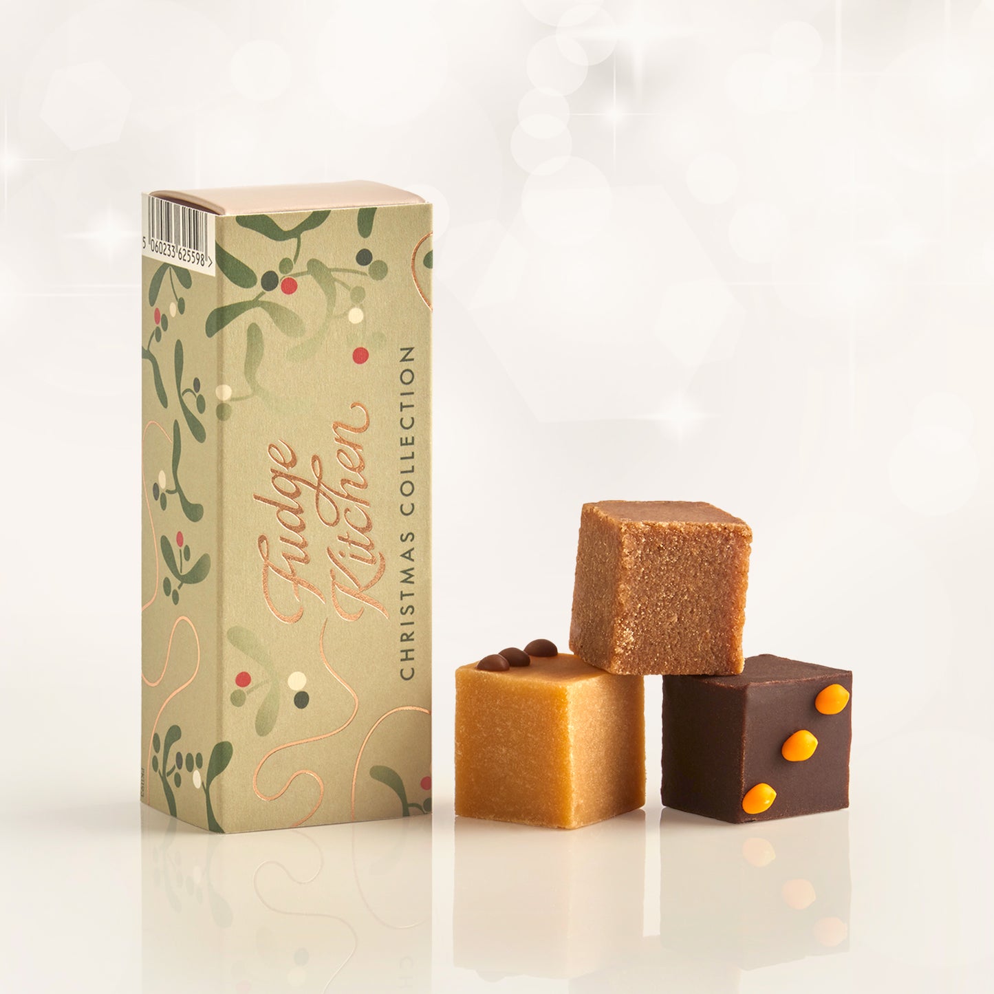 Three pieces of festive fudges stacked in front of the long Fudge Kitchen christmas gift box on a white background.