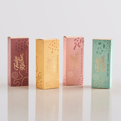 Five colourful fudge slim slider boxes of Fudge Kitchen fudge selections on a light grey background.