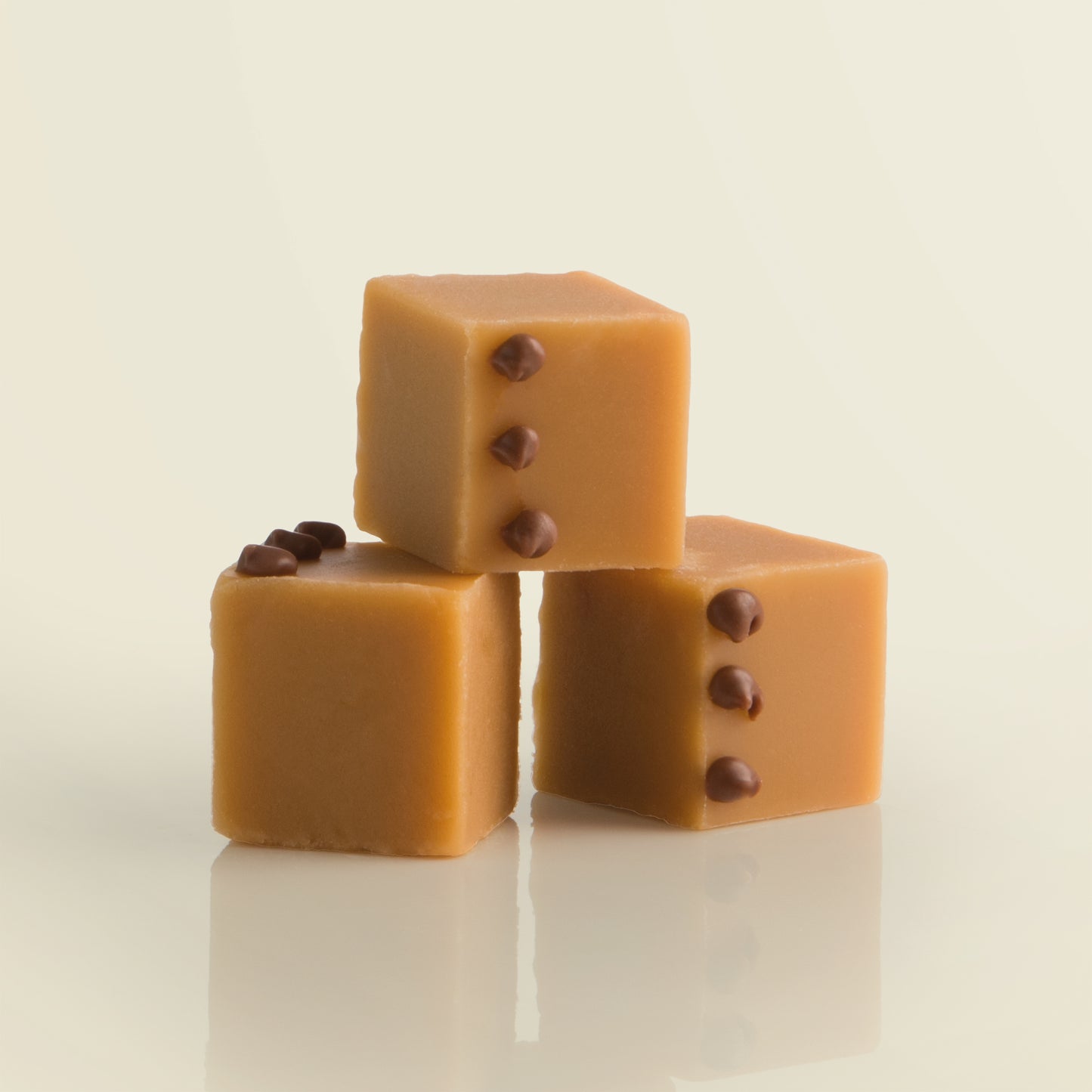 Three cubes of salted caramel fudge with chocolate decoration on a pale yellow background.