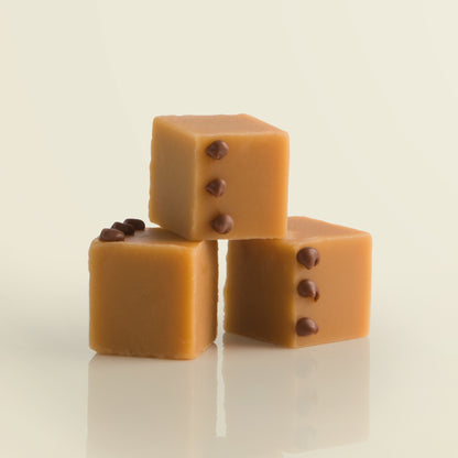 Three cubes of salted caramel fudge with chocolate decoration on a pale yellow background.