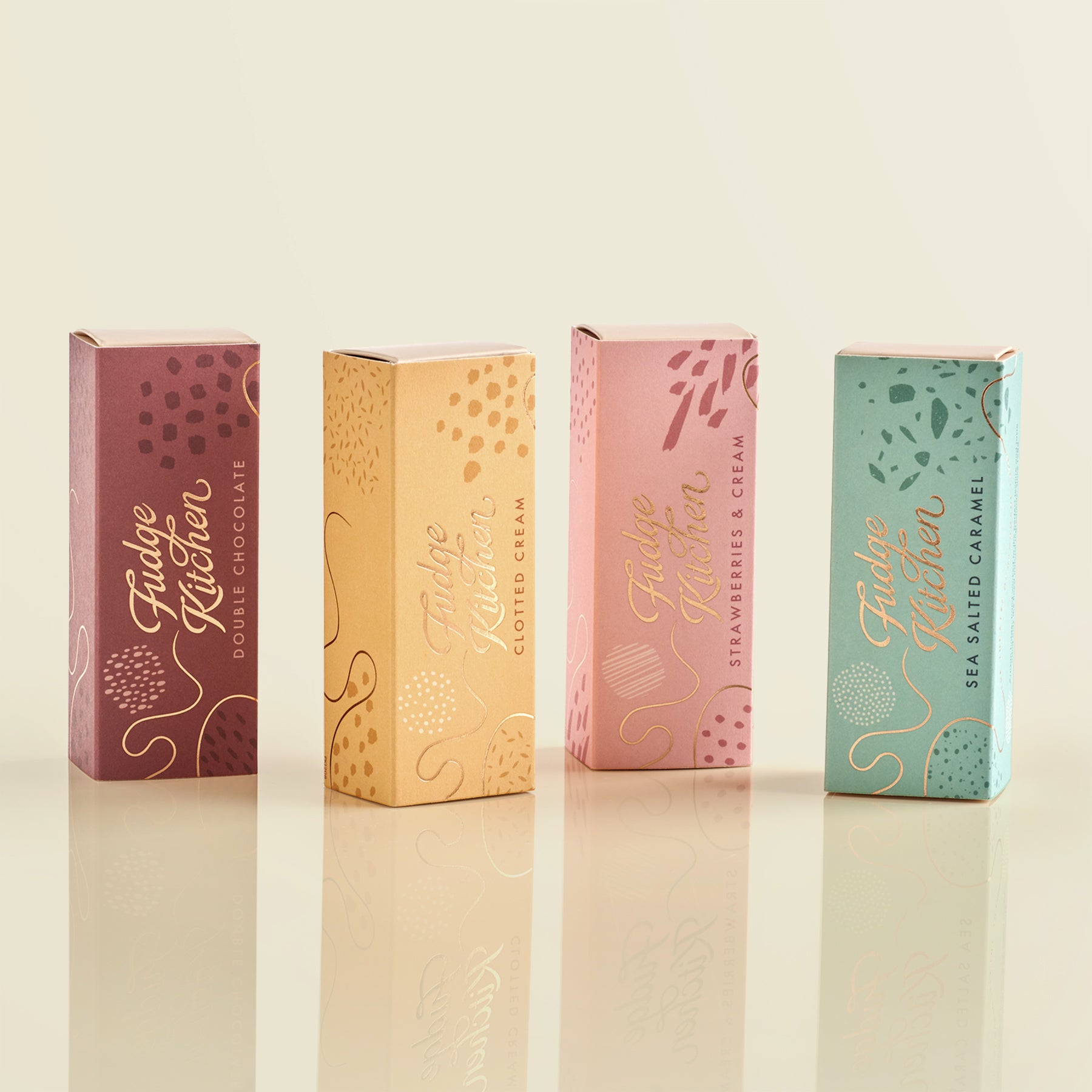 Four colourful fudge slim slider boxes of Fudge Kitchen fudge selections on a pale yellow background.