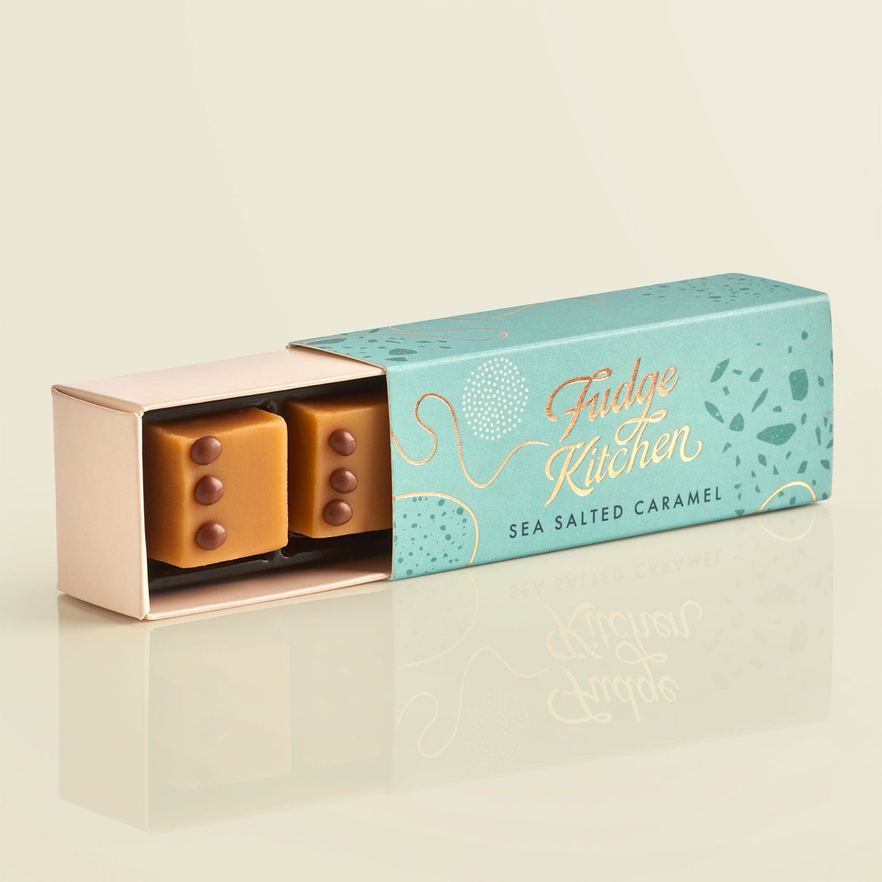 Box of sea salted caramel fudge from Fudge Kitchen on a light beige background, slightly open to reveal a piece of salted caramel.
