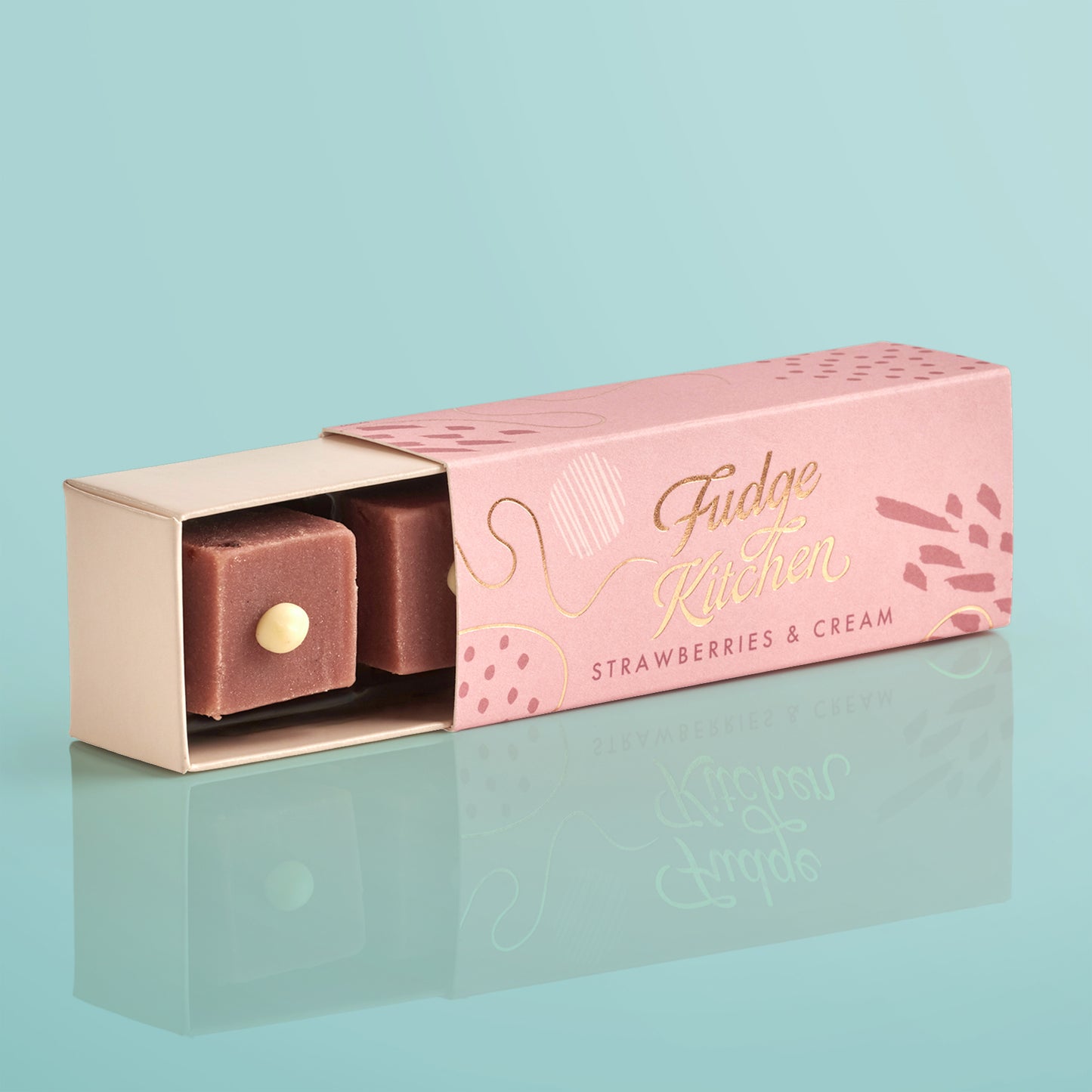 Pink fudge packaging with 'Fudge Kitchen' branding, slightly open to reveal a piece of strawberries & cream fudge on a light blue background.