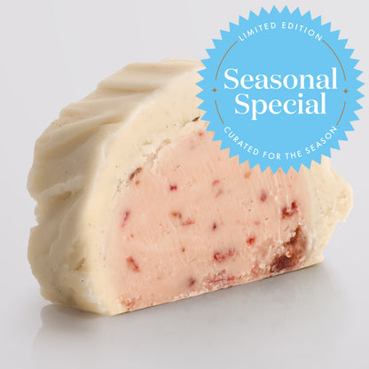 A slice of classic Strawberries & Cream Fudge showing the two layered fudge pairing a base of ripe strawberry fudge with a silky top tier of Madagascan vanilla fudge with a Seasonal Special badge.