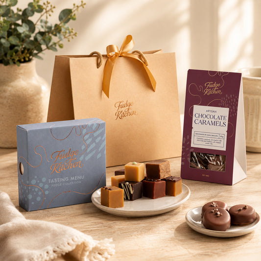 Fudge Kitchen confectionery and premium sweet treats, including boxes, gift bags, a plate of assorted fudges, and a plate of chocolate caramels on a wooden surface.