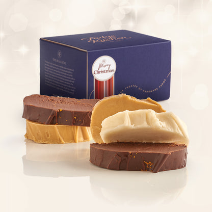 Christmas Fudge Selection showing 5 slices of fresh fudge in christmas flavours ldisplayed on a plain background with a luxury gift box behind with a Christmas Gift with Decorative Seal
